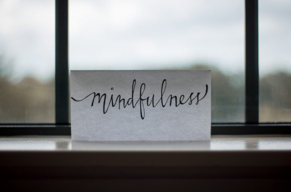 White card with a handwritten phrase "mindfulness" in front of a blurred window.