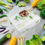 Food box from medimentumHealthFood.store between green vegetables on a wooden background.